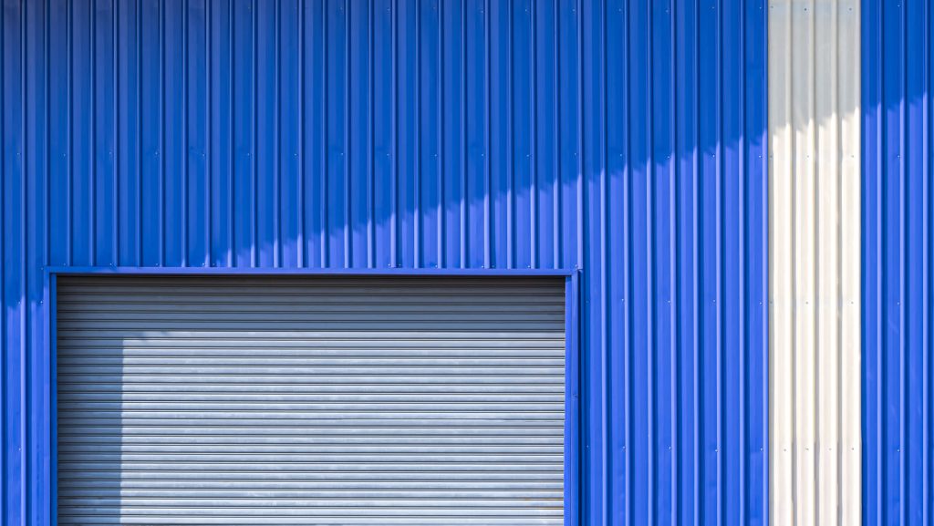 Fachada de un almacén con paredes de metal corrugado en azul y blanco.