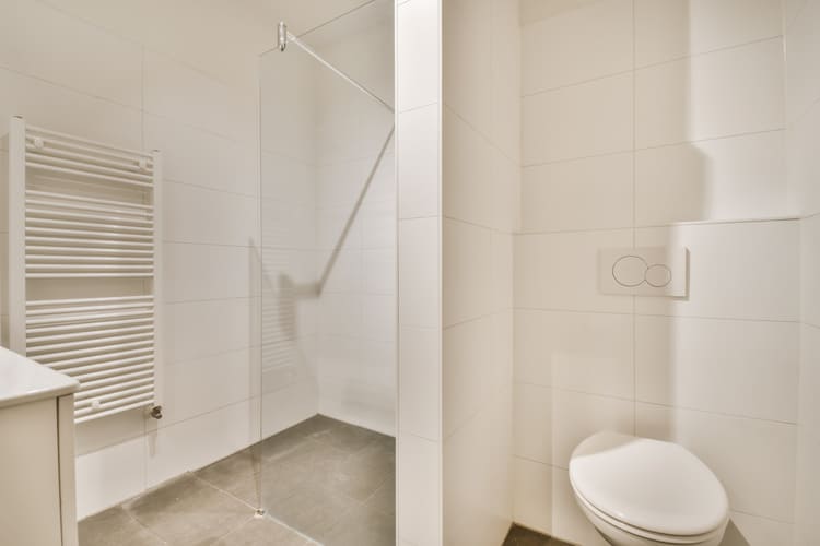 Baño moderno con ducha de vidrio, inodoro y paredes de azulejos blancos.