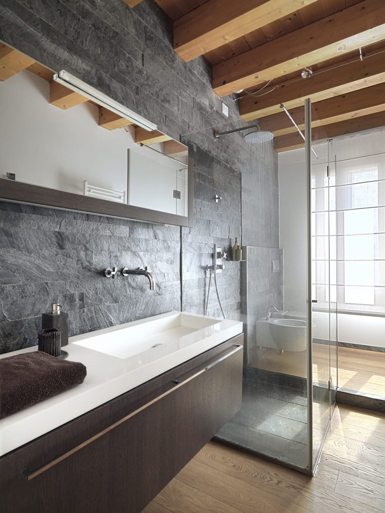 Baño moderno con paredes de pizarra, bañera empotrada y ducha de vidrio.